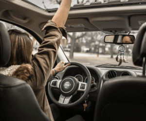 Foto de uma mulher dirigindo um carro com um braço para cima, comprar carro parcelado, consórcio, consórcio de carro, consórcio de moto