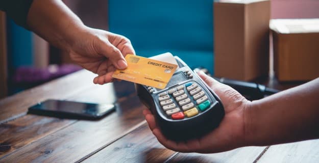 um vendedor segura uma máquina de cartão e um cliente faz a compra por aproximação segurando um cartão de crédito