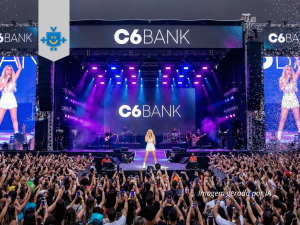 Foto vibrante de um show em estádio lotado à noite. Grandes telões de LED exibem a logo do C6 Bank simbolizando como a conta internacional seria uma cantora pop.