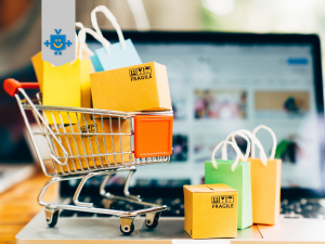 Imagem de um carrinho de compras com várias sacolas na frente de um computador, simbolizando a pesquisa de preços na Internet.